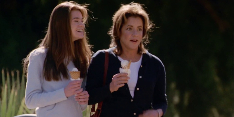 A girl laughs eating an ice cream cone next to her mom.