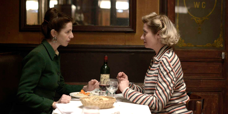 Two women sit across from each other at a French café.