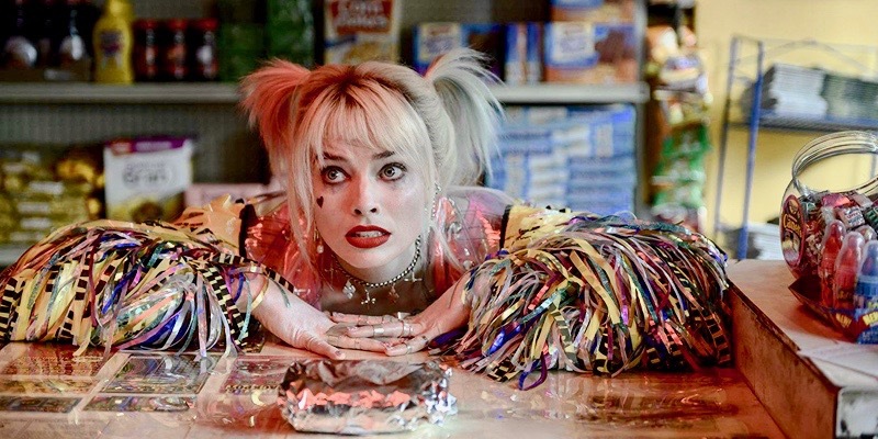Margot Robbie as Harley Quinn leans against a bodega counter.