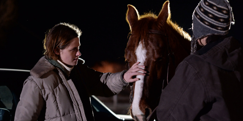 A still from Certain Women. Kristen Stewart pets a horse next to Lily Gladstone.
