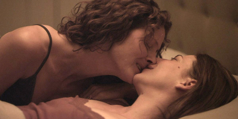 Two middle aged women kiss in bed.
