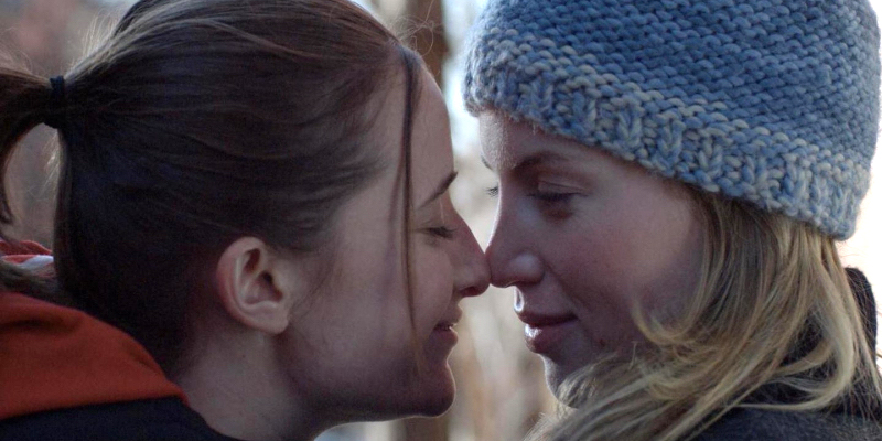 Two women touch noses in winter outfits.