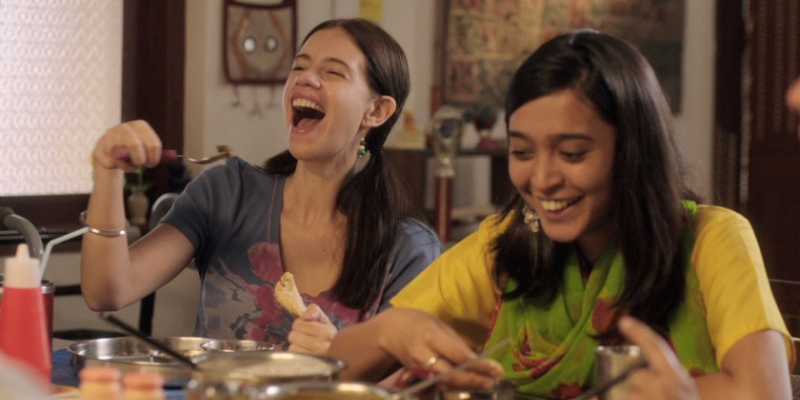 Two girls sit a dinner table laughing.