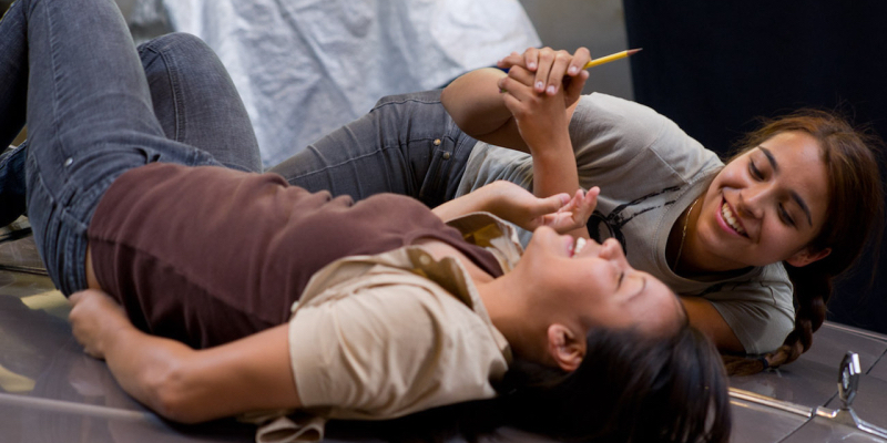 A still from the 46th best lesbian movie of all time Mosquita y Mari. Two girls lie on the hood of a car laughing.