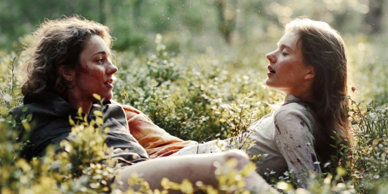 Two girls lie in a field of wildflowers together.