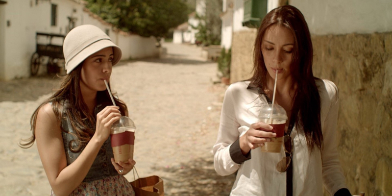 Two women walk next to each other while drinking iced coffee with long straws. 