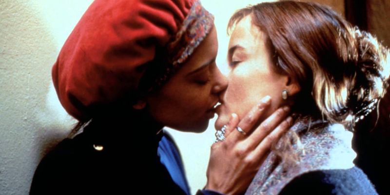 Two women kiss against a wall.