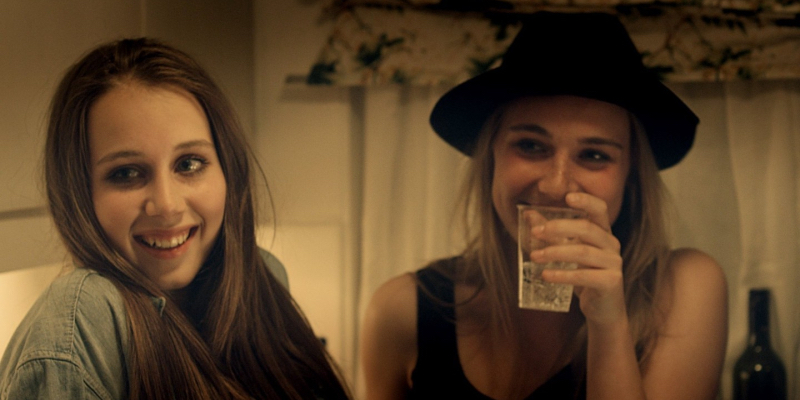 Two girls laugh as one drinks from a glass.