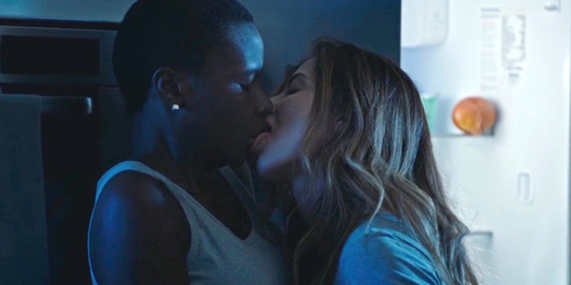 A still from the 23rd best lesbian movie of all time Good Manners. A woman with long hair leans forward and licks the mouth of a woman with short hair.