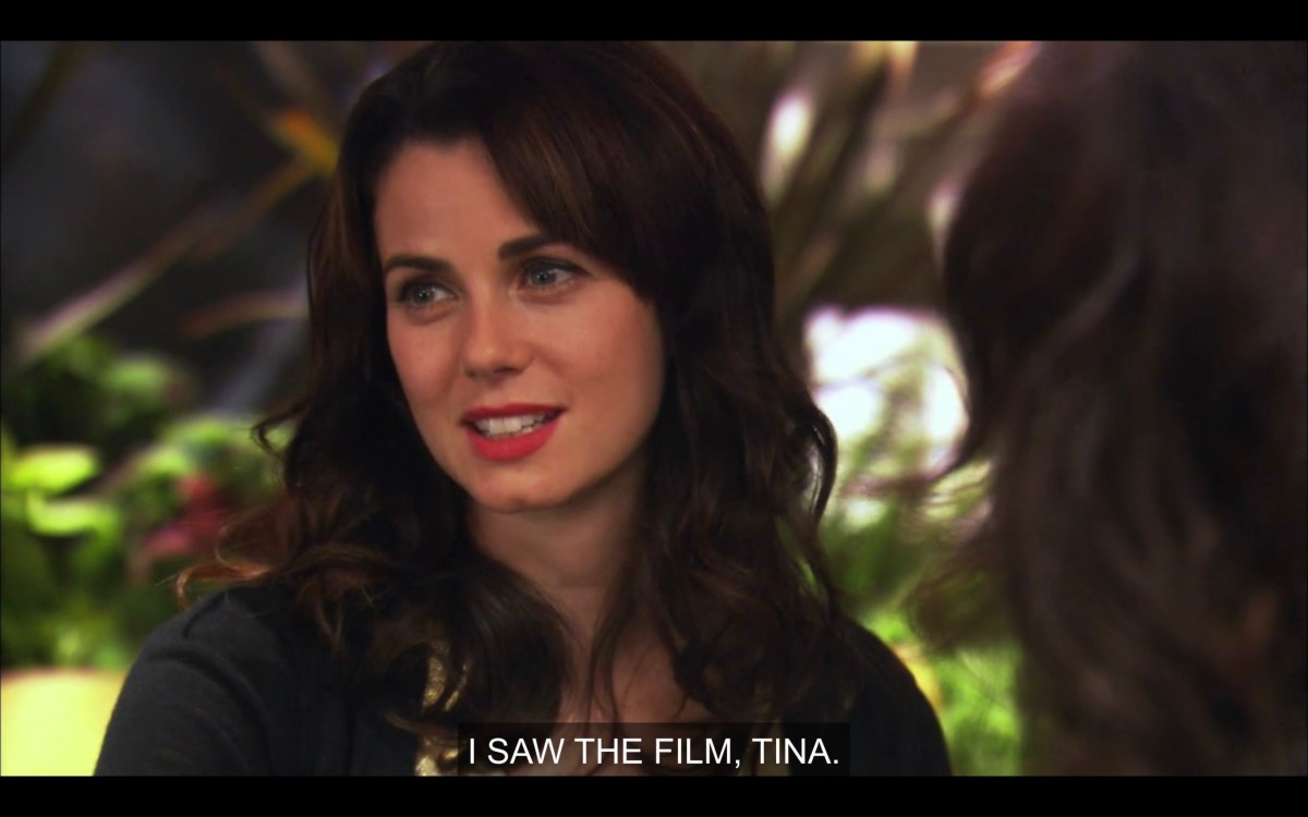 Jenny is sitting outside, wearing red lipstick, her hair down and curled, and a black jacket .She says, "I saw the film, Tina."