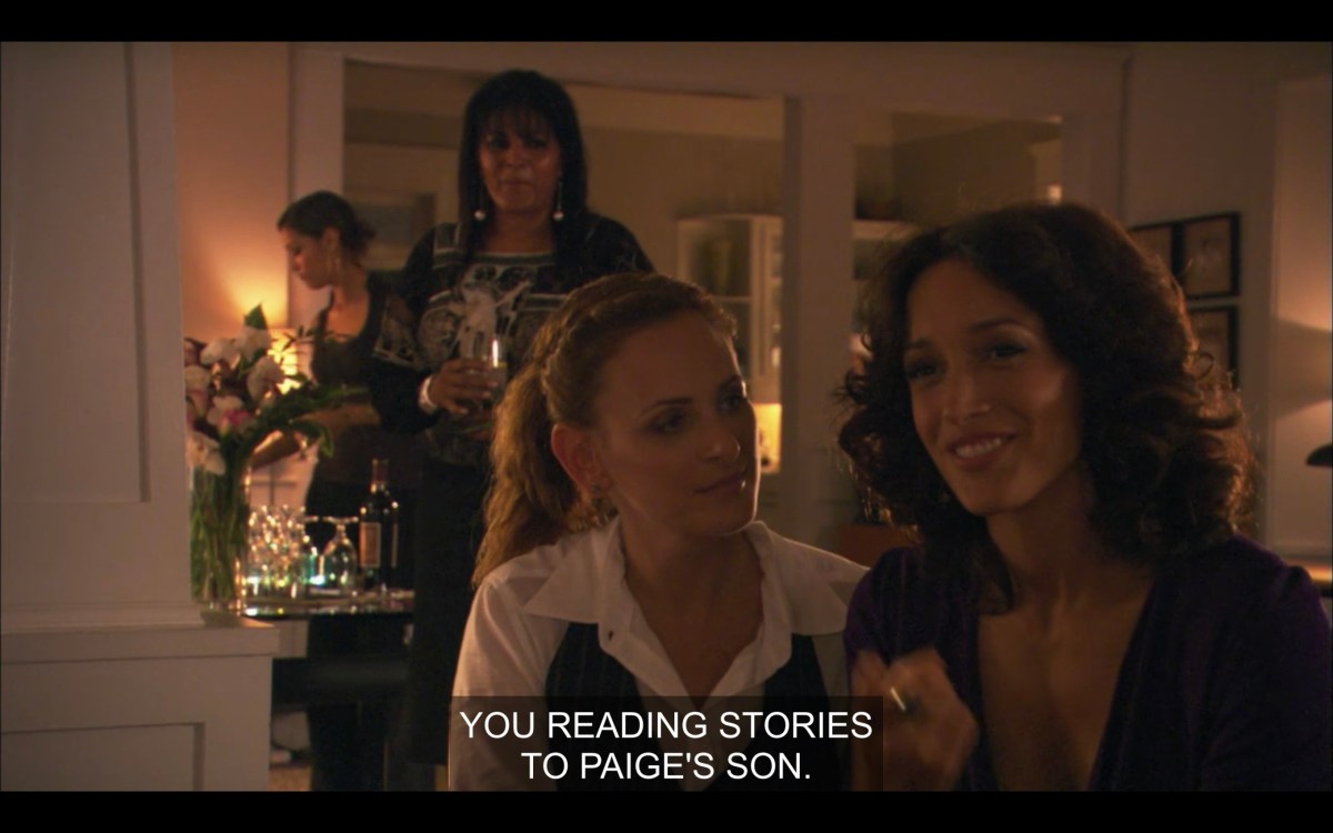 Jodi and Bette sitting on the couch, with Kit and Jenny standing off in the background. Bette says, "You reading stories to Paige's son."