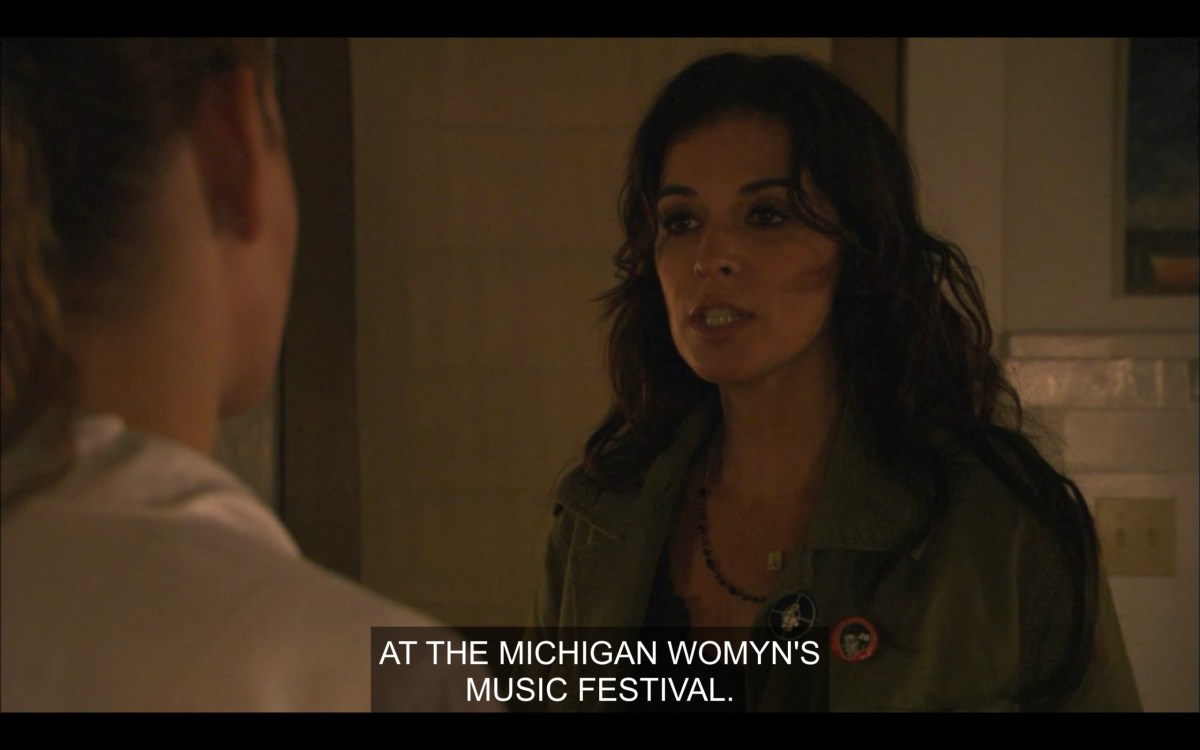 Kate, with long brown hair and wearing a forest green jacket, says, "At the Michigan Womyn's Music Festival."