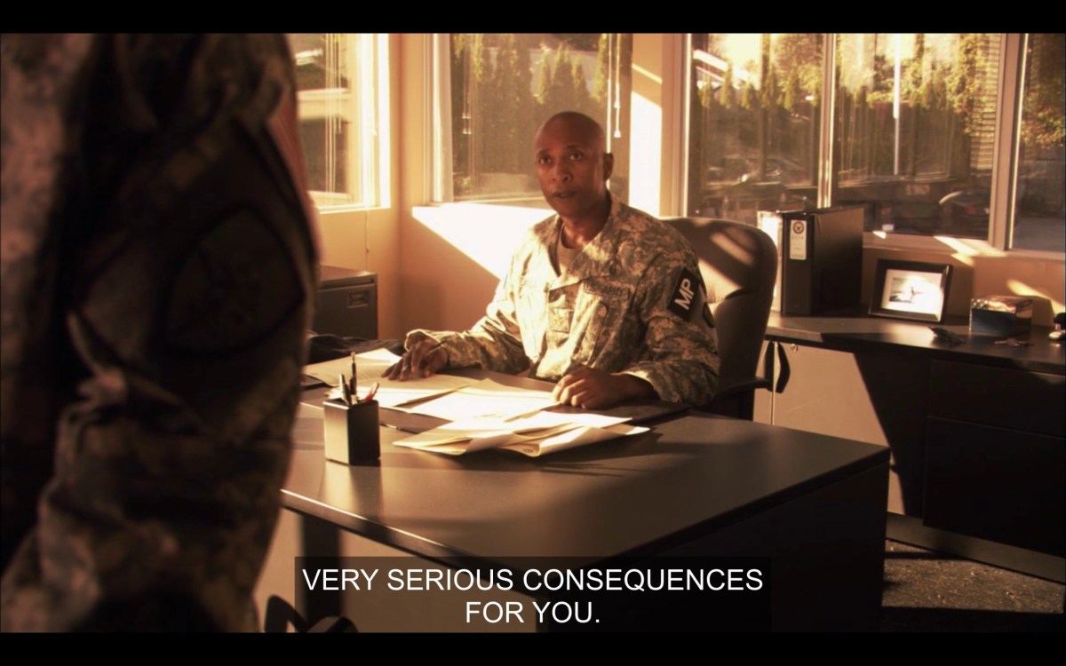 A bald person wearing an army uniform and sitting at a desk. Slightly off camera, Tasha stands in front of the desk with her hands behind her back. The army official says, "Very serious consequences for you."