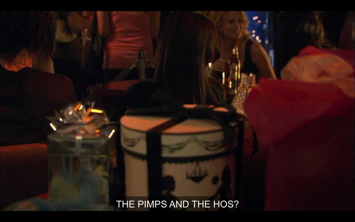 In the foreground, two elaborately wrapped gifts. Behind them, we can see Shane, Alice, Tina, and Jenny sitting around a table together. "The pimps and the hos?"