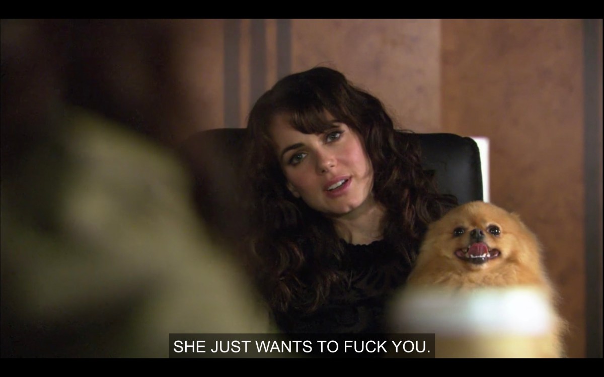 Jenny sits in a high-back black office chair, holding a tan Pomeranian dog on her lap. Her head is tilted to the right, and she says, "She just wants to fuck you."