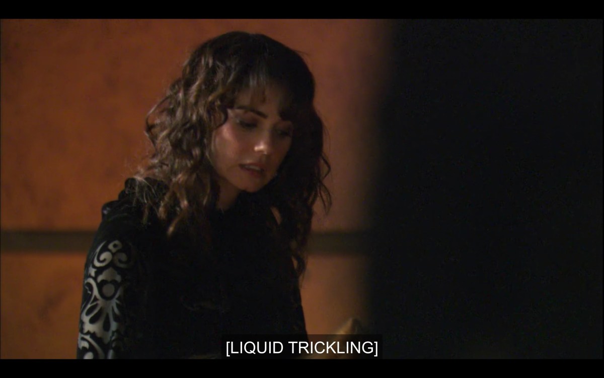 Jenny (with her hair curled and wearing a black dress) looks downwards, averting eye contact. Subtitles read, "[Liquid trickling]"