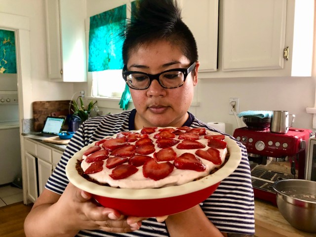 kamala looks at the top of a pie plate piled high with cream and strawberries