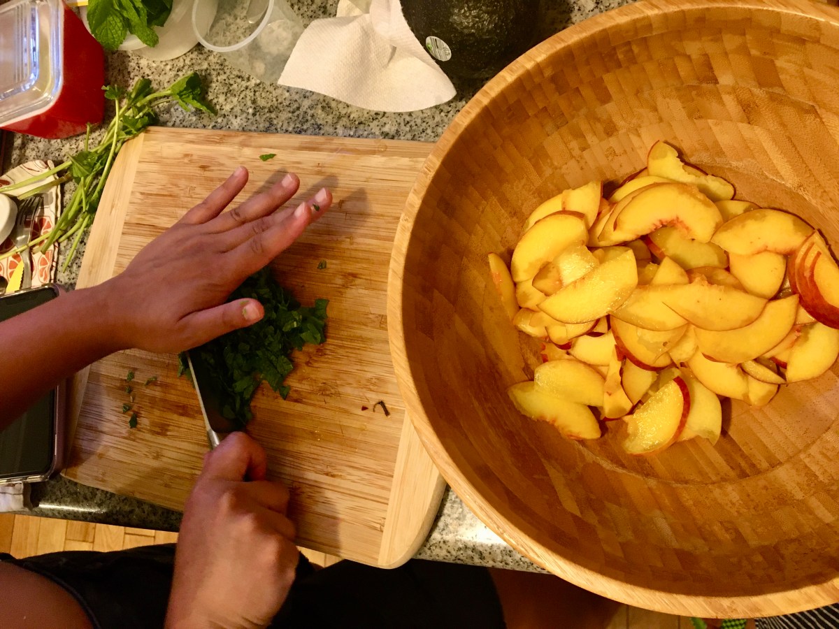 hands chopping herbs beside bowl of peaches