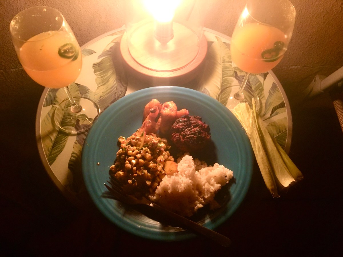 two drinks on a table with a plate of dinner and a light behind it