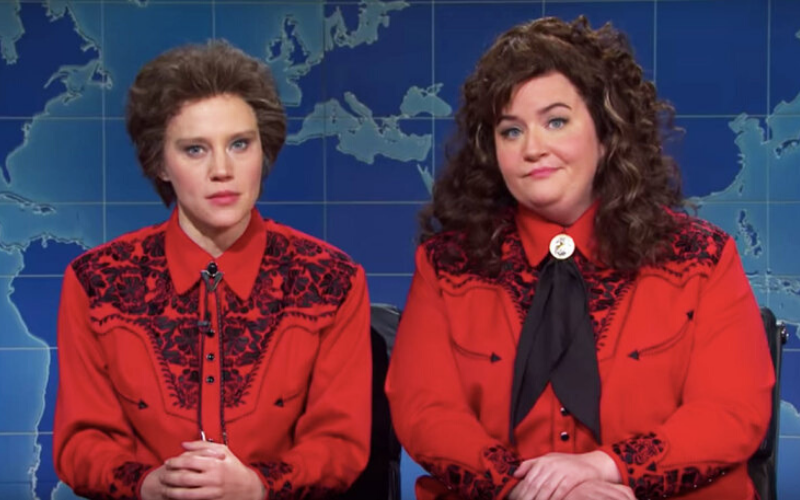 Two white women in curly hair and red western shirts sit at a news desk.