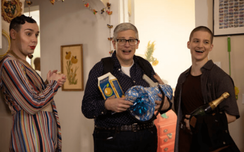 A masculine presenting woman stands between two gender-nonconforming people