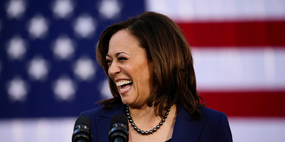 Kamala Harris smiles off to the side in front of the United States flag. Her resemblance to Bette Porter running for Mayor of Los Angeles is uncanny.