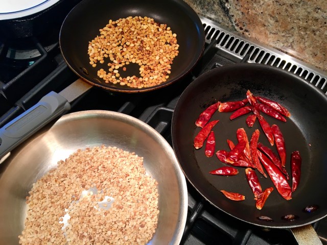three frying pans with charred white urad dal, yellow chana dal, and red chiilies