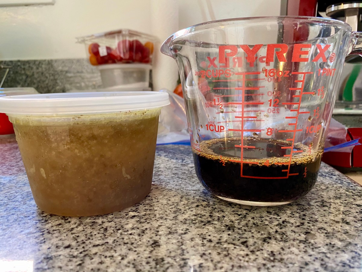 On the counter sits a pint of cloudy homemade chicken broth and a Pyrex measuring glass with has half a cup of brown soy sauce braising liquid in it