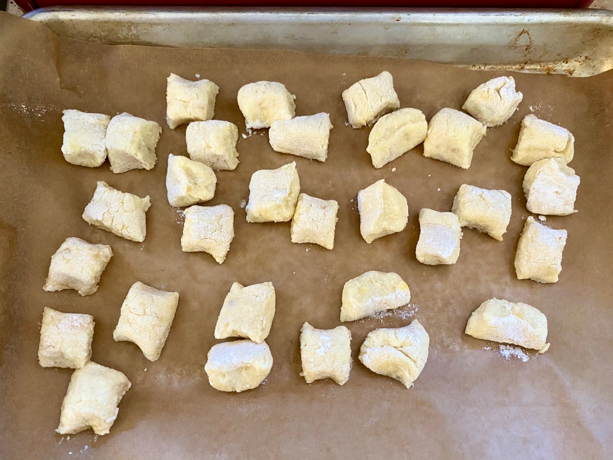 A shot of a half baking sheet, where recently cut piece of gnocchi are scattered, like little mishhapen pillows, and awaiting their boil