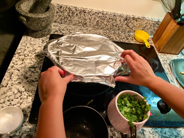 two hands press foil over the top of a dutch oven to seal the top