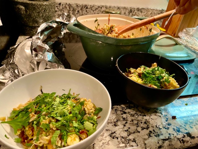 a bowl of yellow rice topped with herbs getting served from a dutch oven on the stove top