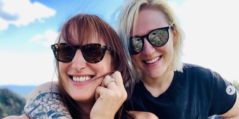 Jen Richards and Rebekah Cheyne are posing for their engagement photo. Both are wearing sunglasses and Jen's hand is in a fist near her cheek, showing off her engagement ring. They are both smiling like "Love wins" after all!