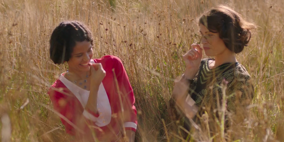 Gemma Arterton as Alice and Gugu Mbatha-Raw as Vera, sitting together in a field laughing in the film Summerland.