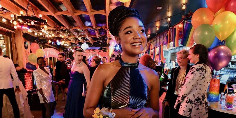 Kat Edison from "The Bold Type" wears a rainbow full length gown in a bar filled with rainbow balloons.