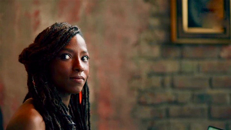 Nova Bordelon from "Queen Sugar" sits thoughtfully alone in a chair in front of a brick wall that is full of rich, warm tones.