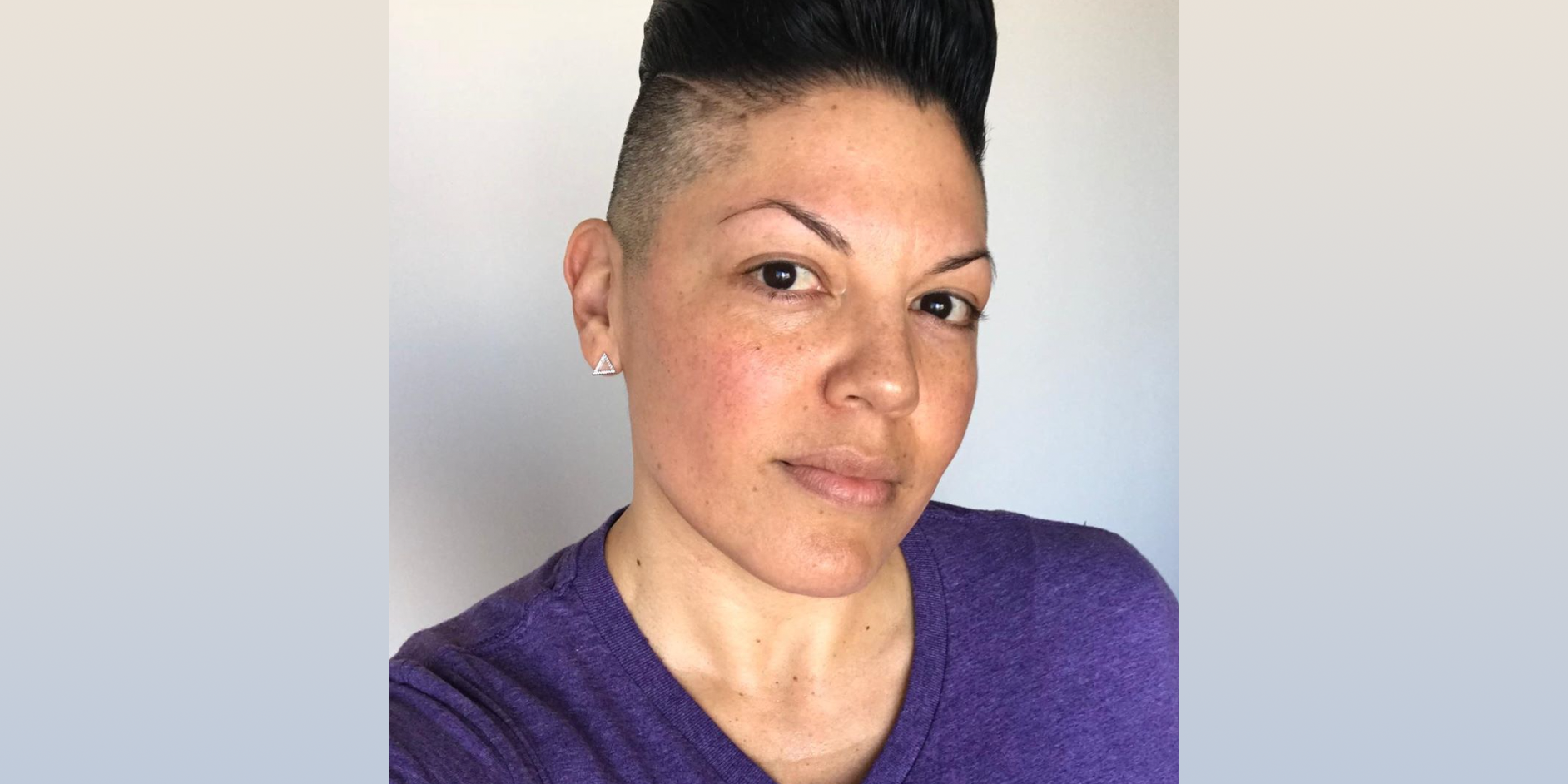 A photo of Sara Ramirez in a purple t-shirt on the day that they came out as non-binary.