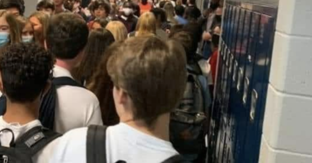 A photo taken on a smartphone by a teenager at school shows a crowded hallway of students standing shoulder to shoulder, breathing on each other, with very few wearing masks.