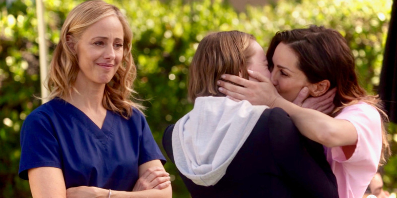 Station 19's captain Maya Bishop and Grey's Anatomy's Dr. Carina DeLuca share a make out in the sunshine as Grey's Anatomy recent resident bisexual, Dr. Teddy Altman, looks on proudly.