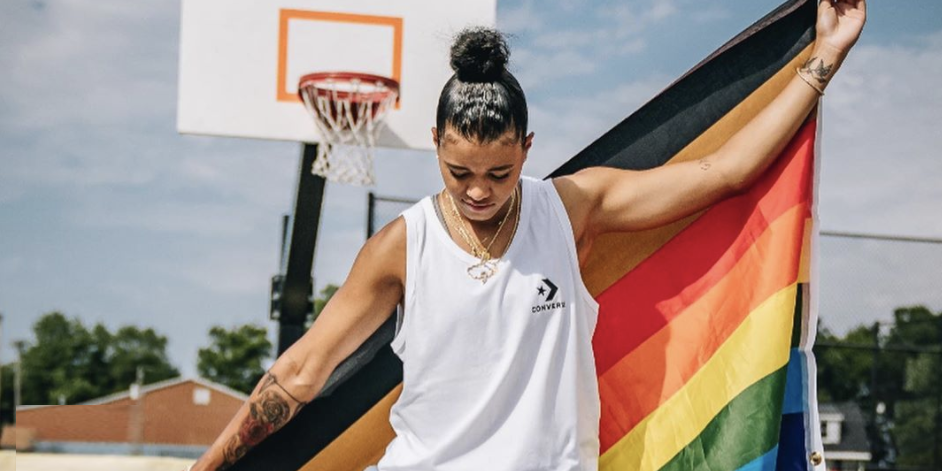 Natasha Cloud holds a Pride/Black Lives Matter flag on an outdoor basketball court.