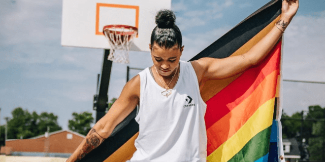 Natasha Cloud holds a Pride/Black Lives Matter flag on an outdoor basketball court.