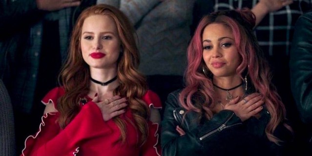 Toni and Cheryl from Riverdale stand beside each other with their hands over their hearts.