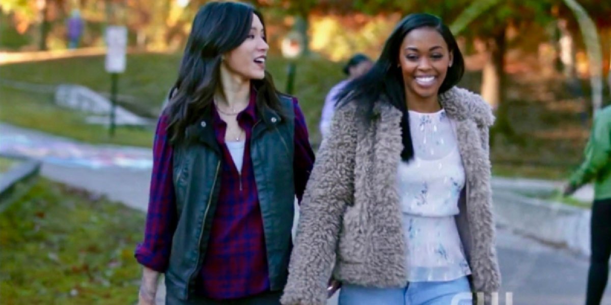 Grace Choi and Anissa Pierce from "Black Lightning" hold hands and smile on a fall date in the park.