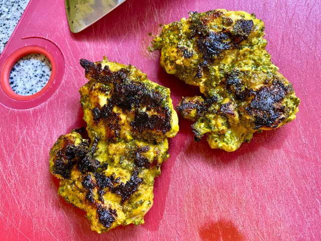 a red cutting board with two yellow-tinted chicken thighs with a browning on the outside