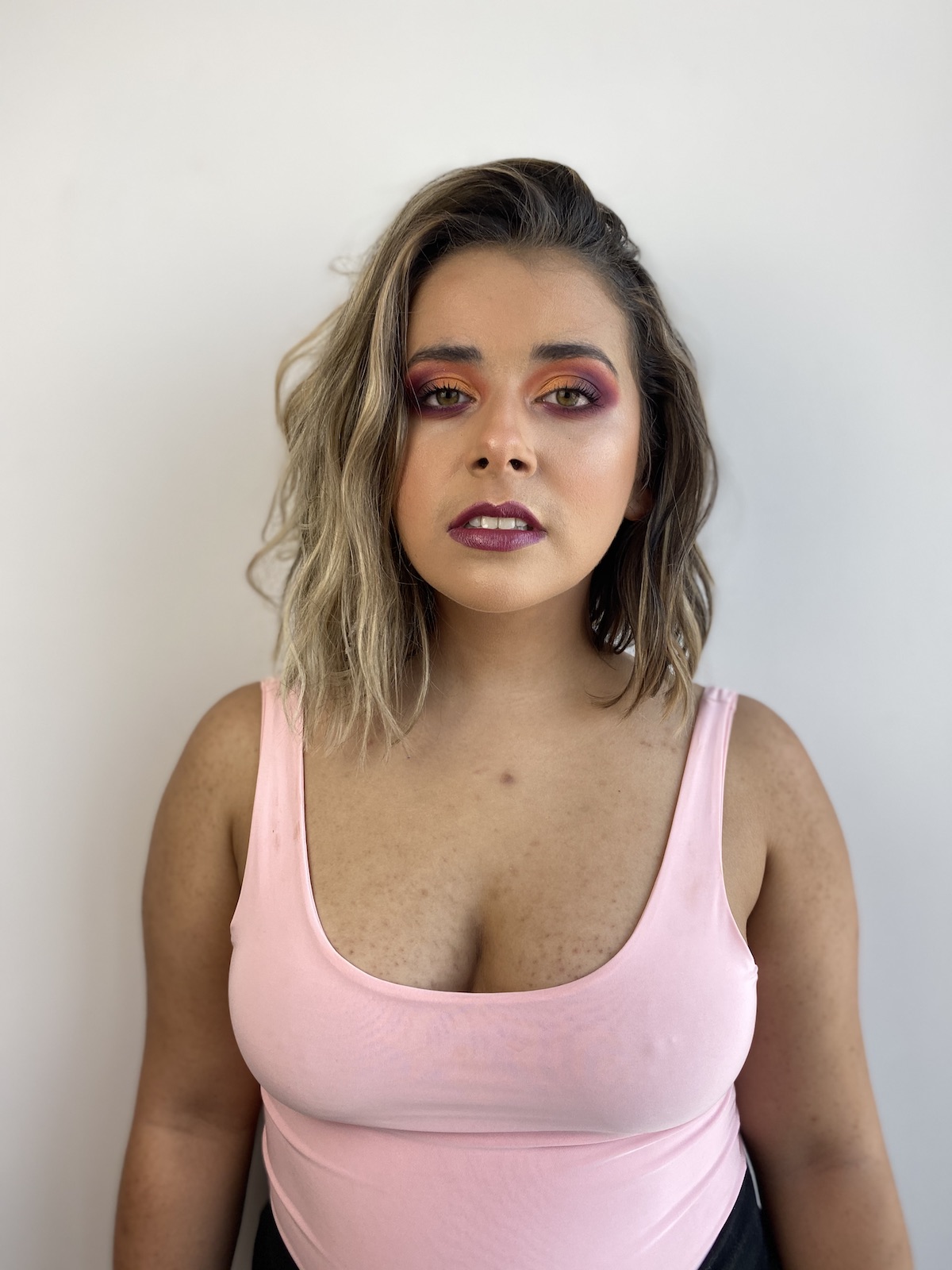 The author, Olivia Zayas Ryan, stares directly at the camera with a full face of dramatic makeup in a magenta and orange color scheme. Her expression is neutral.