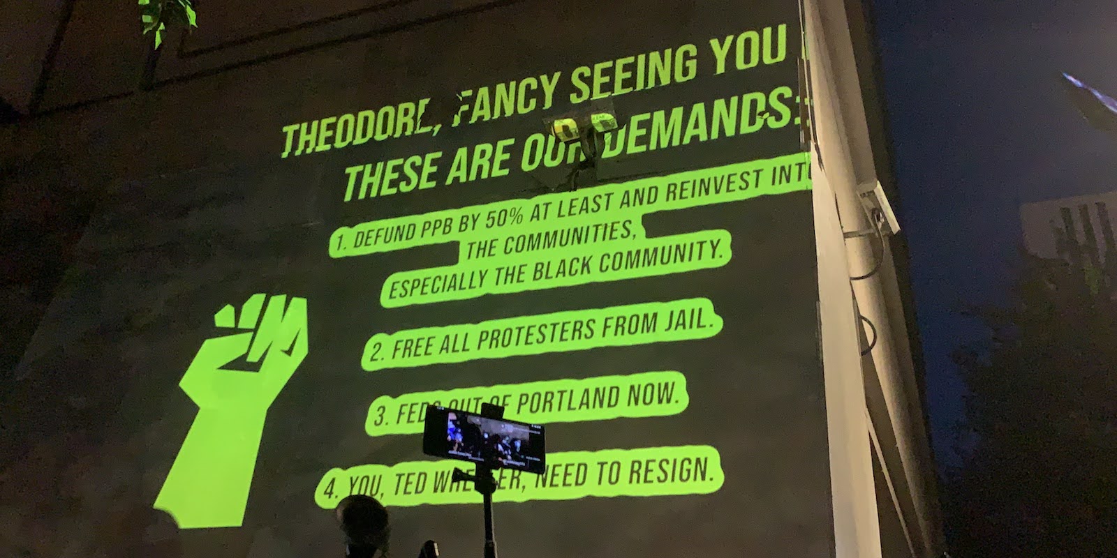 Protesters project a list of demands onto the wall of the Portland Police Bureau's downtown headquarters as Mayor Ted Wheeler attempts to dialog with members of the crowd on July 22