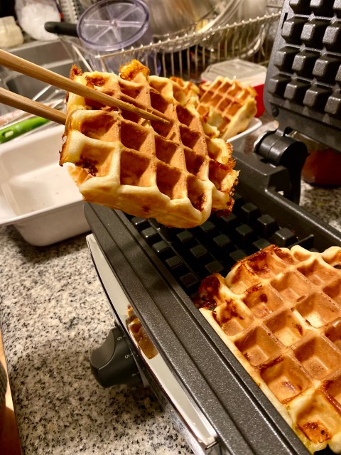 cripsy waffles being pulled hot out of a waffle iron with chopsticks