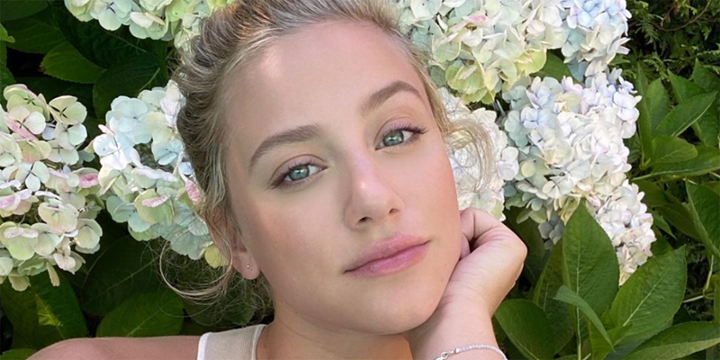 Bisexual star Lili Reinhart takes a selfie in front of white flowers.
