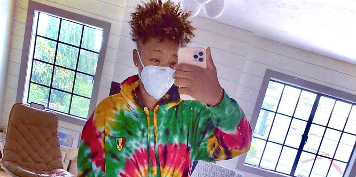 Samira Wiley poses for a selfie in her mirror with a mask on. She is wearing a tie dye sweatshirt and growing out her signature haircut.