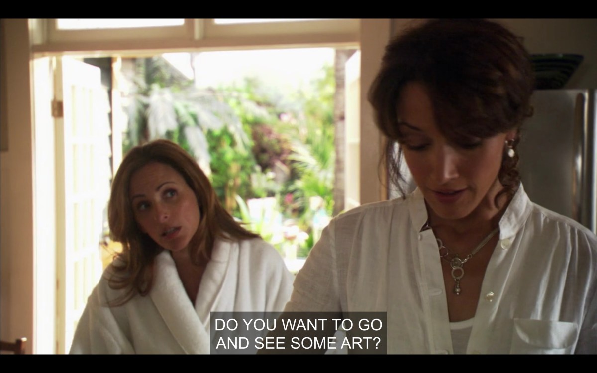 Jodi in a fluffy robe asks Bette, in a white shirt looking down, if she wants to go see some art
