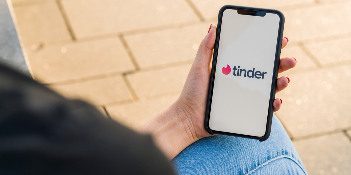 A seated woman holds a mobile phone loading Tinder